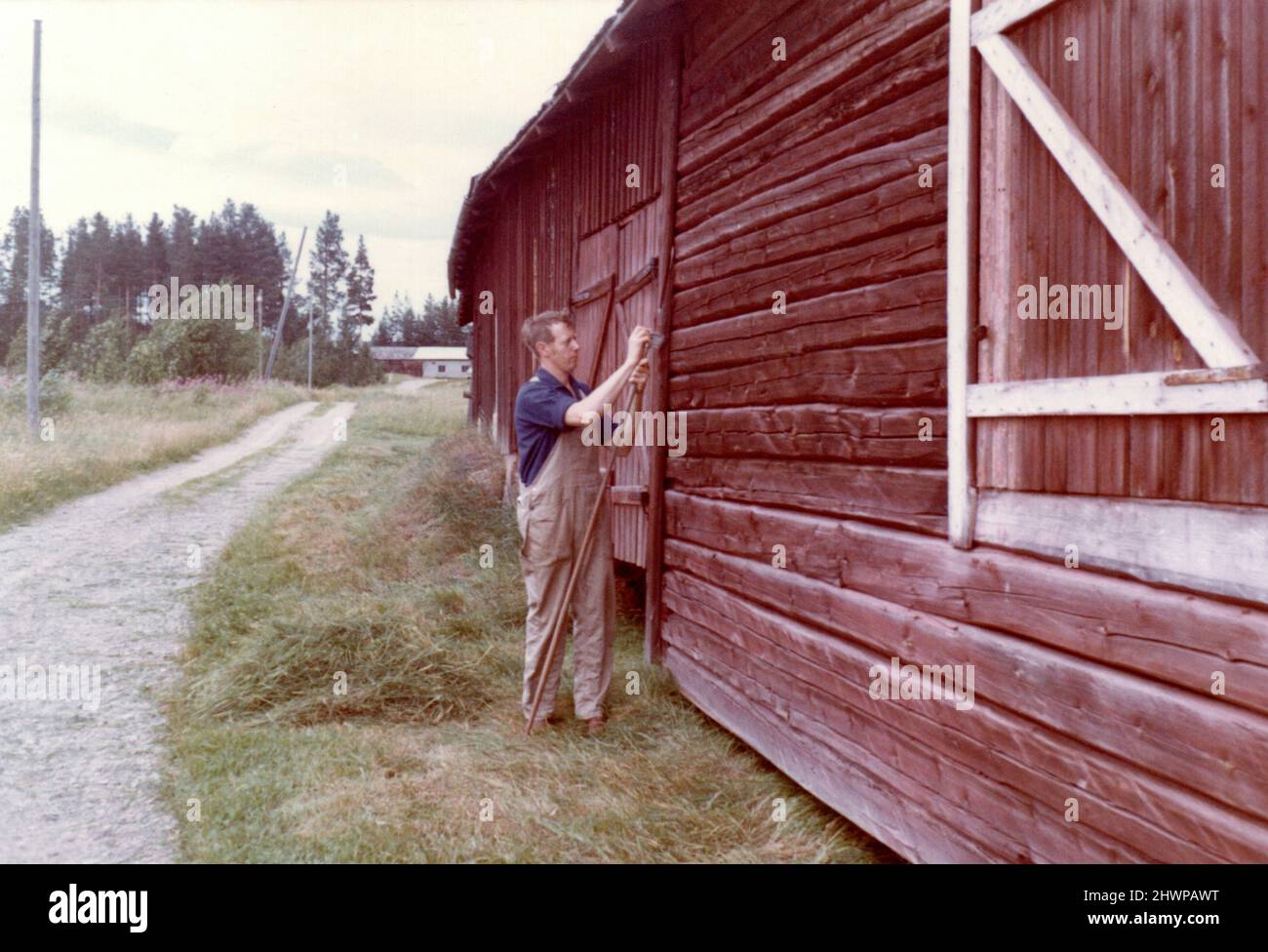 Fotografía original de los años 70 del hombre en la calle fuera del tradicional edificio de madera roja falu en el entorno rural, Suecia Foto de stock
