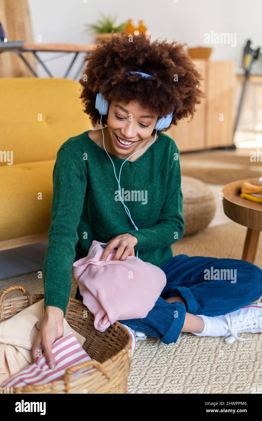 Mujer joven afro escuchando música y doblando ropa en casa Fotografía de  stock - Alamy