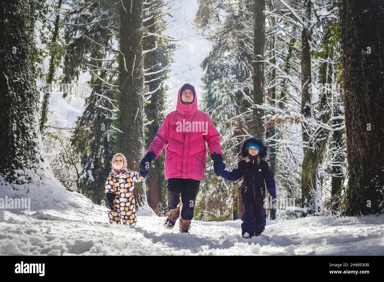 Padre con hijas caminando en el bosque nevado en el día soleado Foto de stock