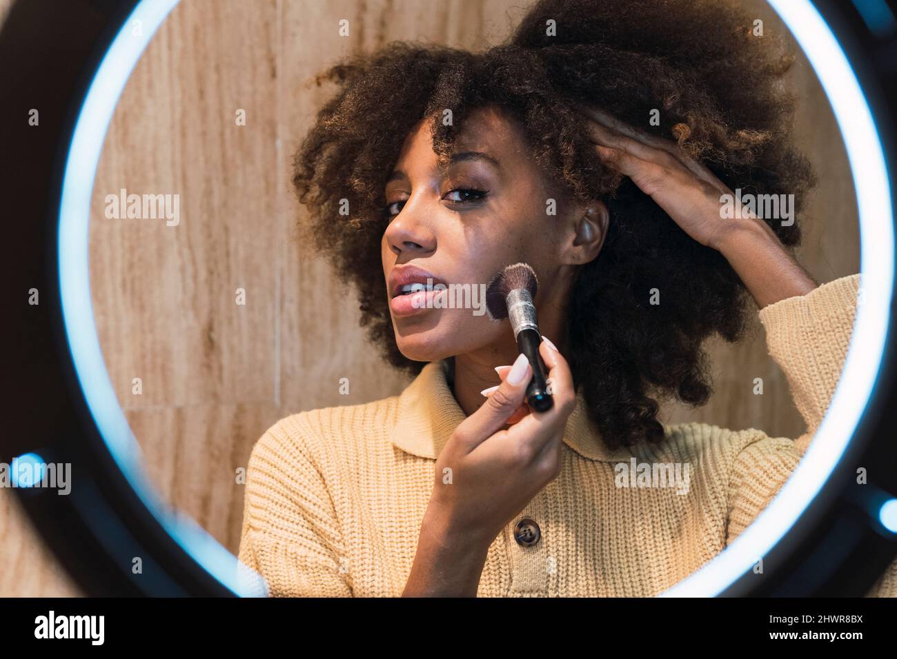 Joven influencer aplicando blusher en la mejilla delante de la luz del anillo Foto de stock