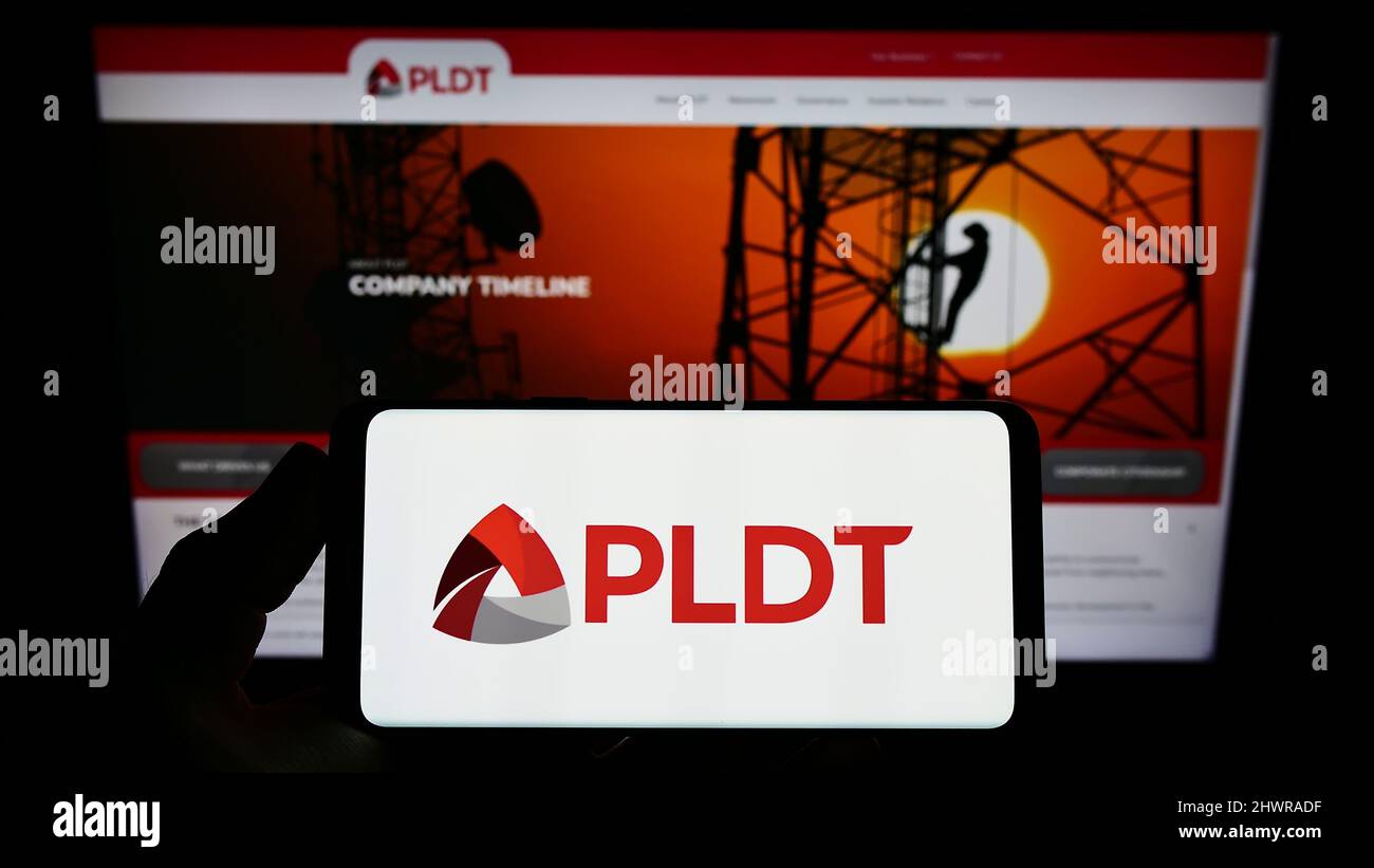 Persona que sostiene el smartphone con el logotipo de la compañía filipina de telecomunicaciones PLDT Inc. En la pantalla delante del sitio web. Enfoque en la pantalla del teléfono. Foto de stock