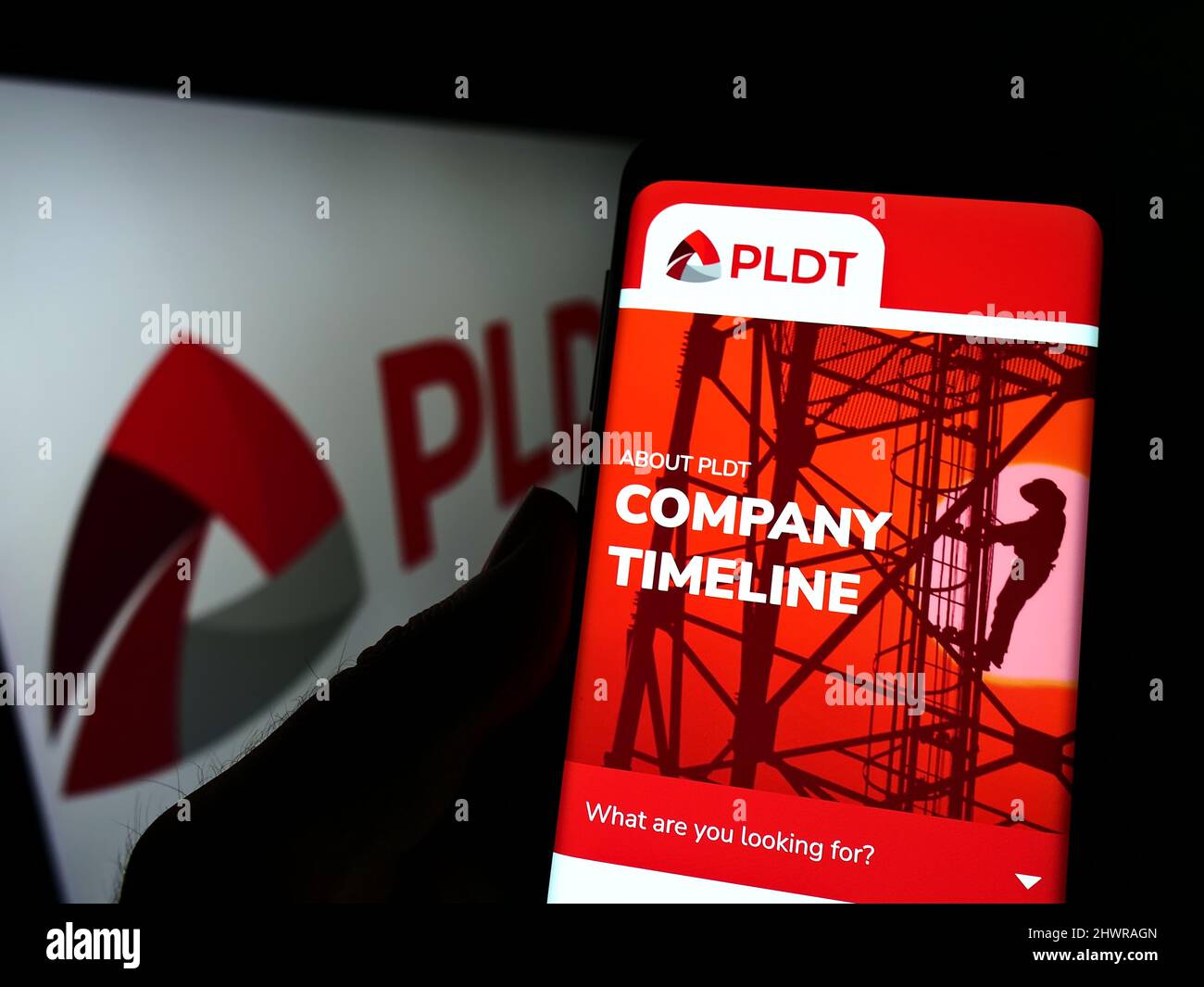 Persona que sostiene el smartphone con el Web site de la compañía filipina de las telecomunicaciones PLDT Inc. En la pantalla con el logo. Enfoque en el centro de la pantalla del teléfono. Foto de stock