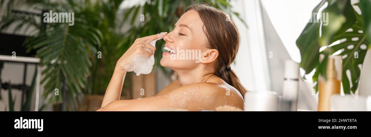 Linda mujer joven divirtiéndose, jugando con burbujas de jabón mientras se baña en un spa tropical Foto de stock