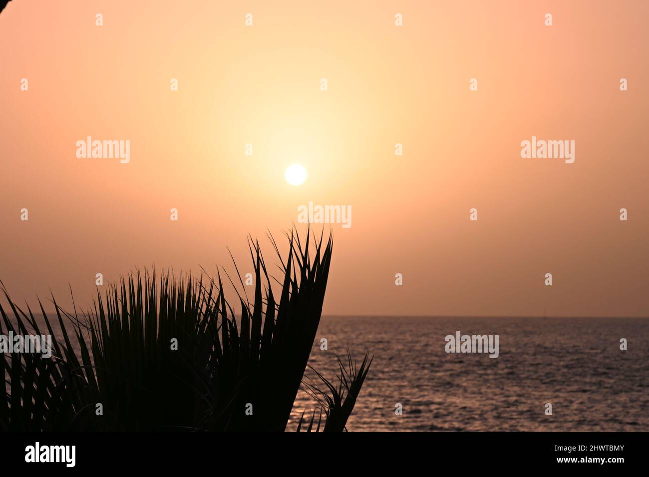 Una vista de la puesta de sol sobre el Océano Atlántico, en Costa Adeje, Tenerife, España, con las relucientes vigas del sol que se reflejan en el océano Foto de stock