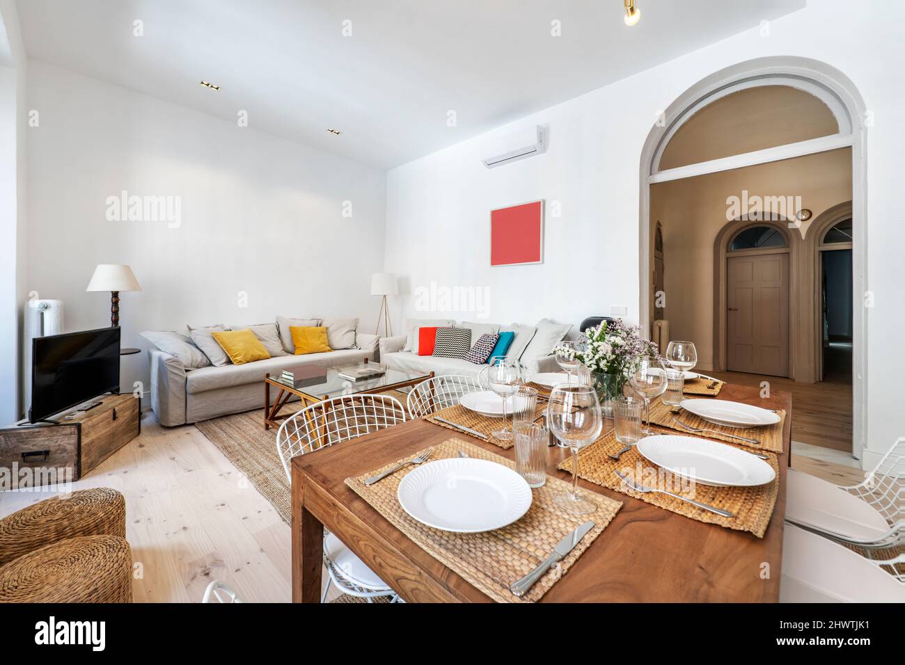 Bonita sala de estar con grandes sofás tapizados en tela gris, mesa de  comedor de madera con vajilla y acceso a la habitación con un arco de medio  punto Fotografía de stock -