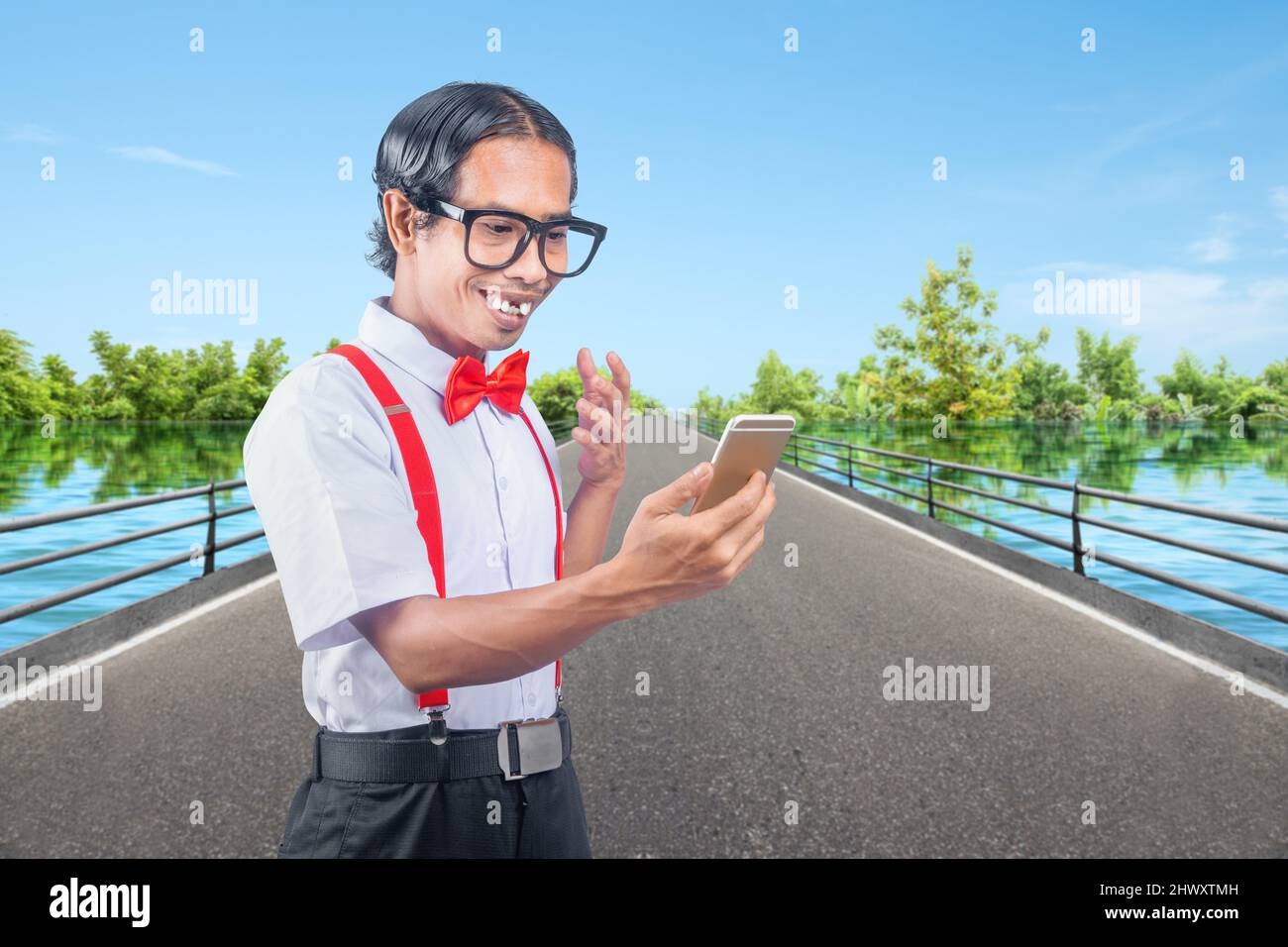 Nerd asiático con una cara fea que sostiene el teléfono móvil en la calle Foto de stock