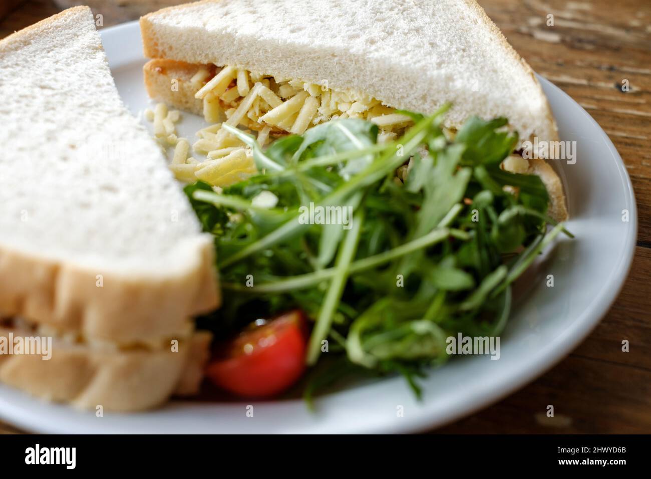 Un queso cheddar recién hecho, rallado, sándwich, hecho con pan blanco. Se sirve con una guarnición de ensalada en un plato blanco Foto de stock