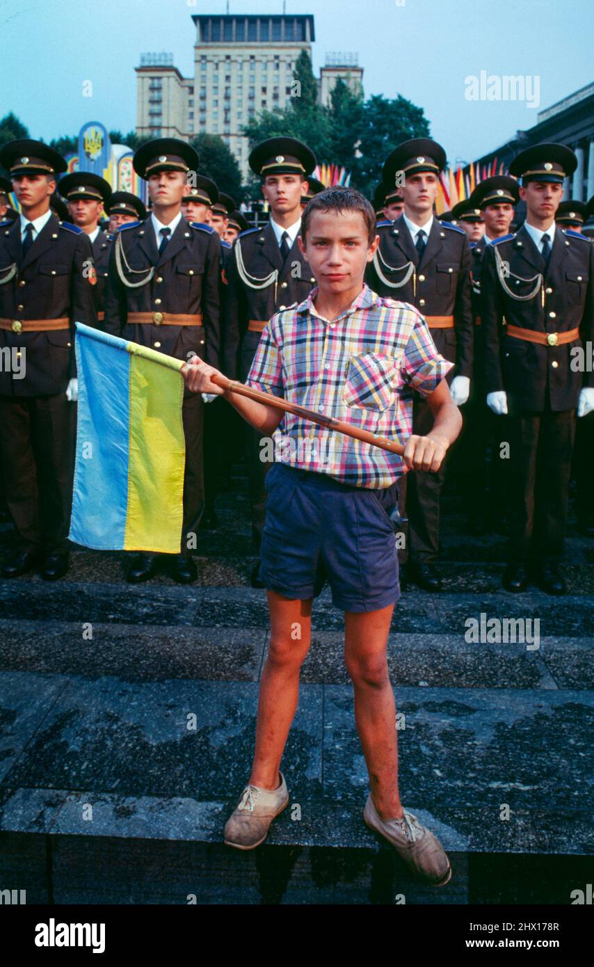 Joven con bandera azul y amarilla ucraniana frente a soldados en la plaza Maidan (ucraniano: Майдан Незалежності) durante la celebración del primer aniversario de la independencia ucraniana en Kiev, Ucrania, 1992. Foto de stock