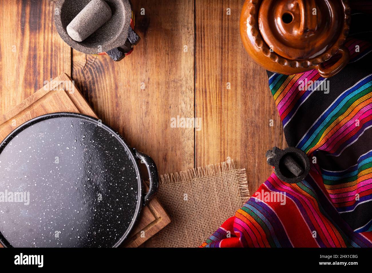 Cocina mexicana utensilios de cocina. Colorista tejido tradicional, comal de peltre, olla de barro y molcajete sobre mesa rústica de madera. Vista superior con espacio de copia Foto de stock