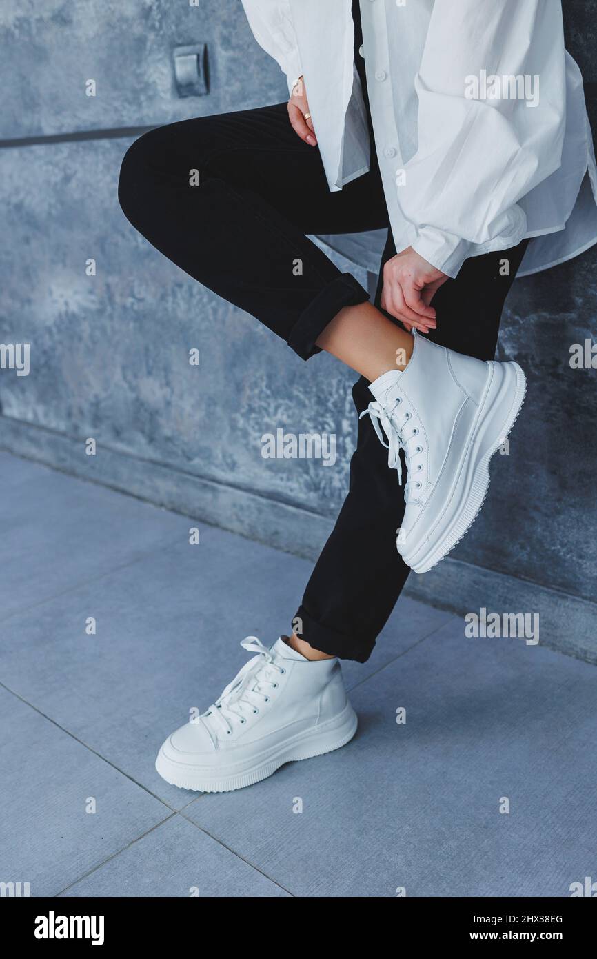 Piernas para mujer en pantalones negros y sneakers de piel blanca. Estilo  moderno e informal. Nueva colección de zapatillas Fotografía de stock -  Alamy