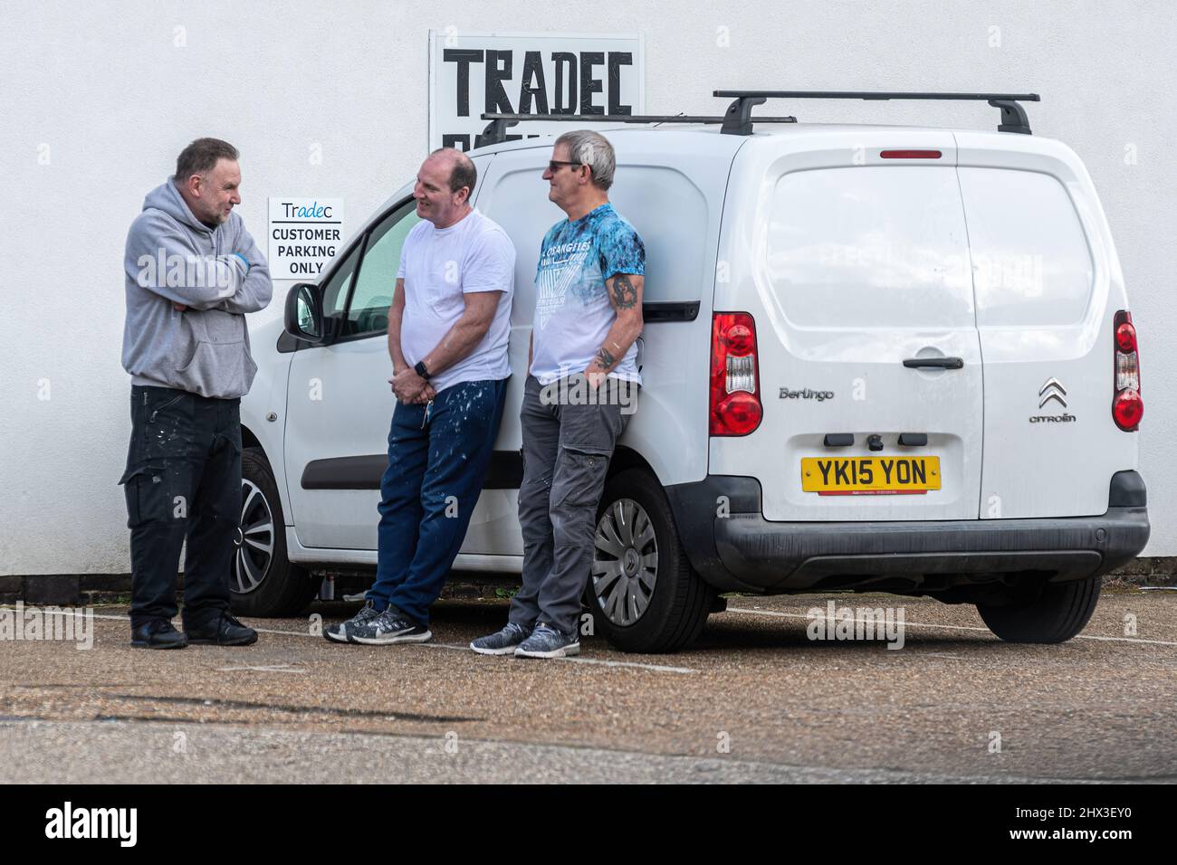 Tres hombres de trabajo pintores de pie en una furgoneta charlando y bromeando en el aparcamiento de un negocio de pintura y decoración, Reino Unido vida laboral cotidiana Foto de stock