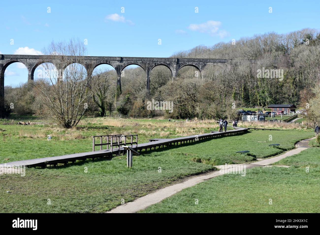 Gente caminando a lo largo del paseo marítimo de madera en el parque rural de Porthkerry frente al viaducto del ferrocarril, Barry, Glamourgan, Gales Foto de stock