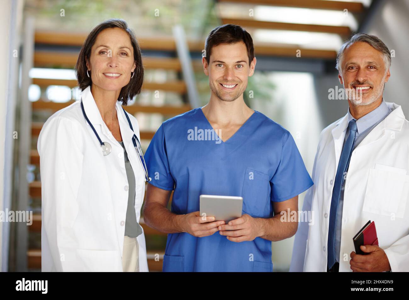 Estaban aquí para ayudar. Un retrato recortado de un guapo joven médico de pie con una tableta entre dos de sus colegas. Foto de stock