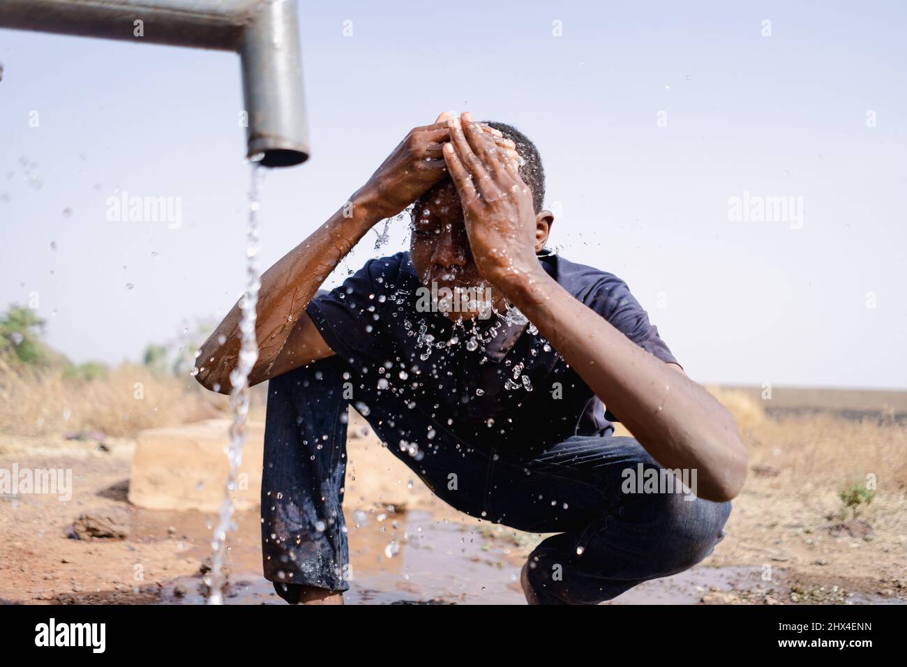 Niño africano joven lavando su cara en el grifo de la aldea: Repetición del Día Mundial del Agua Foto de stock