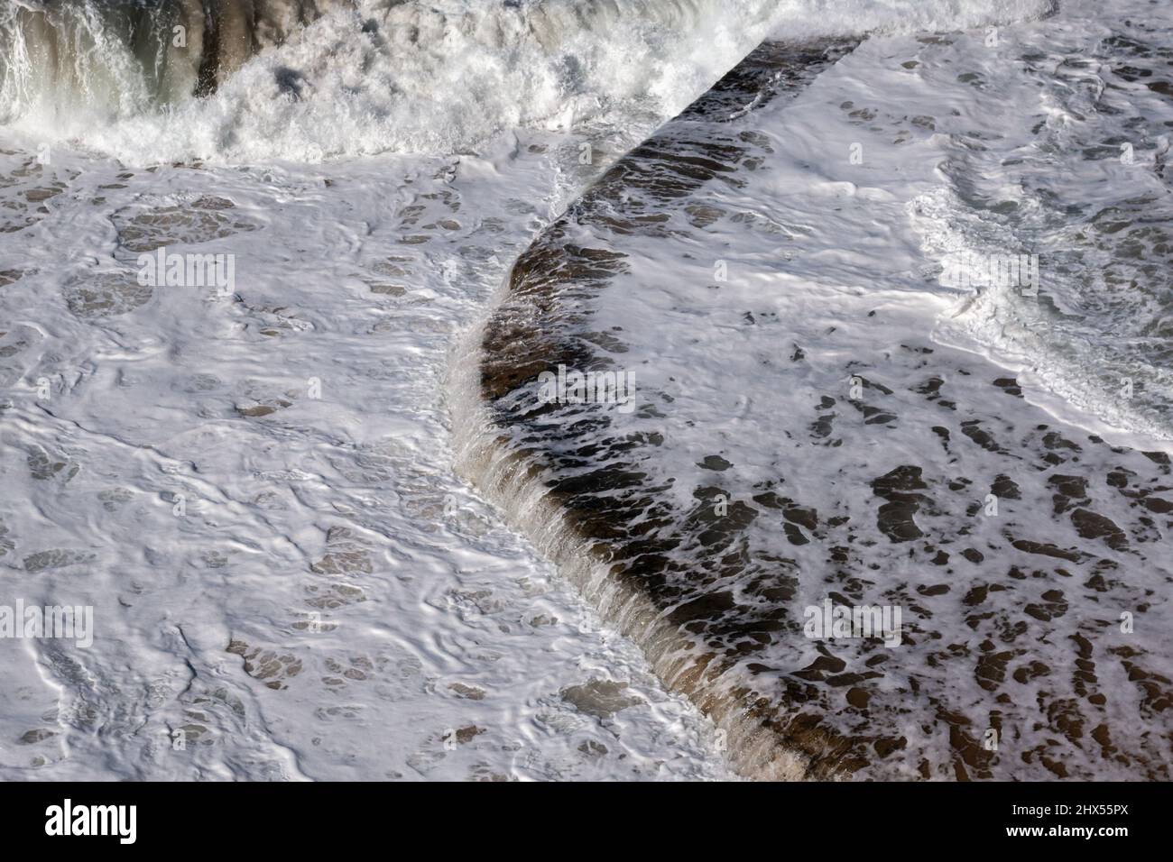 Las olas de marea del Océano Atlántico fluyen sobre el borde de una piscina de agua salada en la costa de Sintra en Portugal Foto de stock