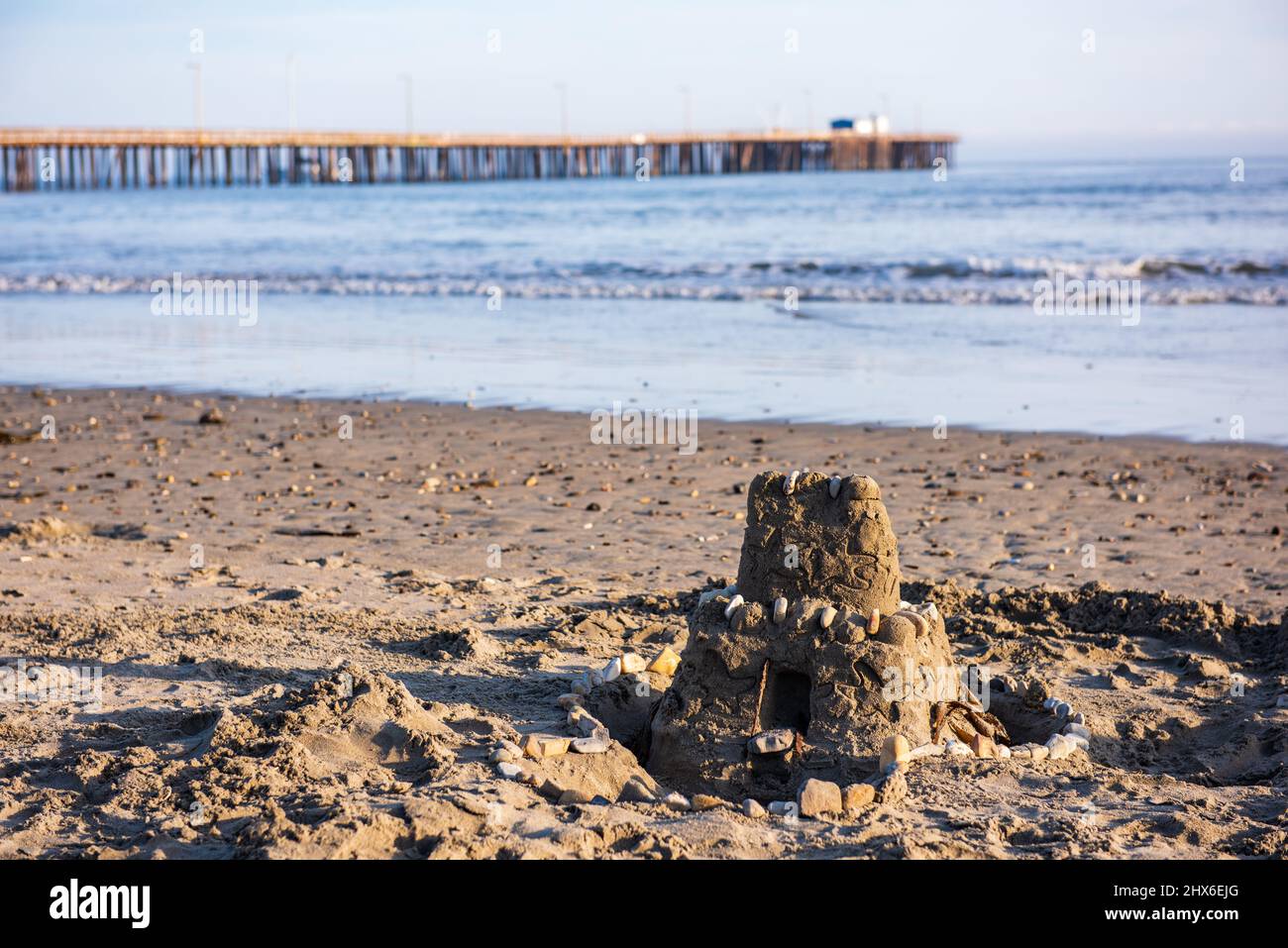 Castillo de arena de dos pisos decorado con conchas en la orilla de Avila Beach, con muelle en el fondo. Foto de stock
