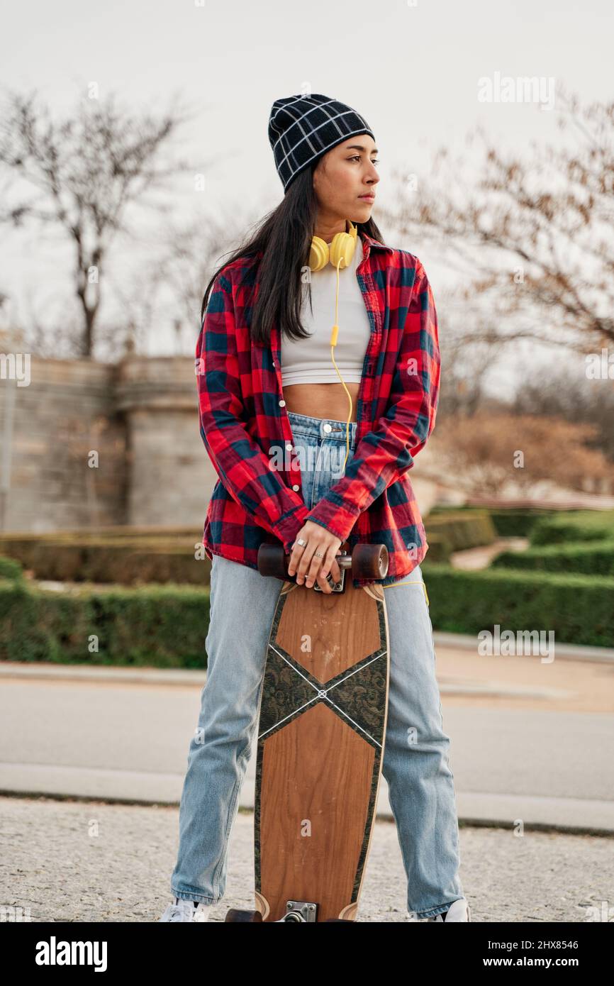 Hermosa joven hipster posando con skateboard. Mujer hispana con ropa informal Fotografía de stock - Alamy