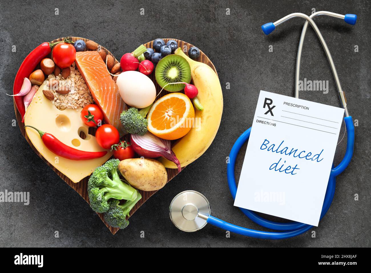 Una dieta sana y equilibrada. Alimentos saludables en una tabla cortante de madera en forma de corazón, estetoscopio y prescripción. Concepto de alimentación saludable Foto de stock
