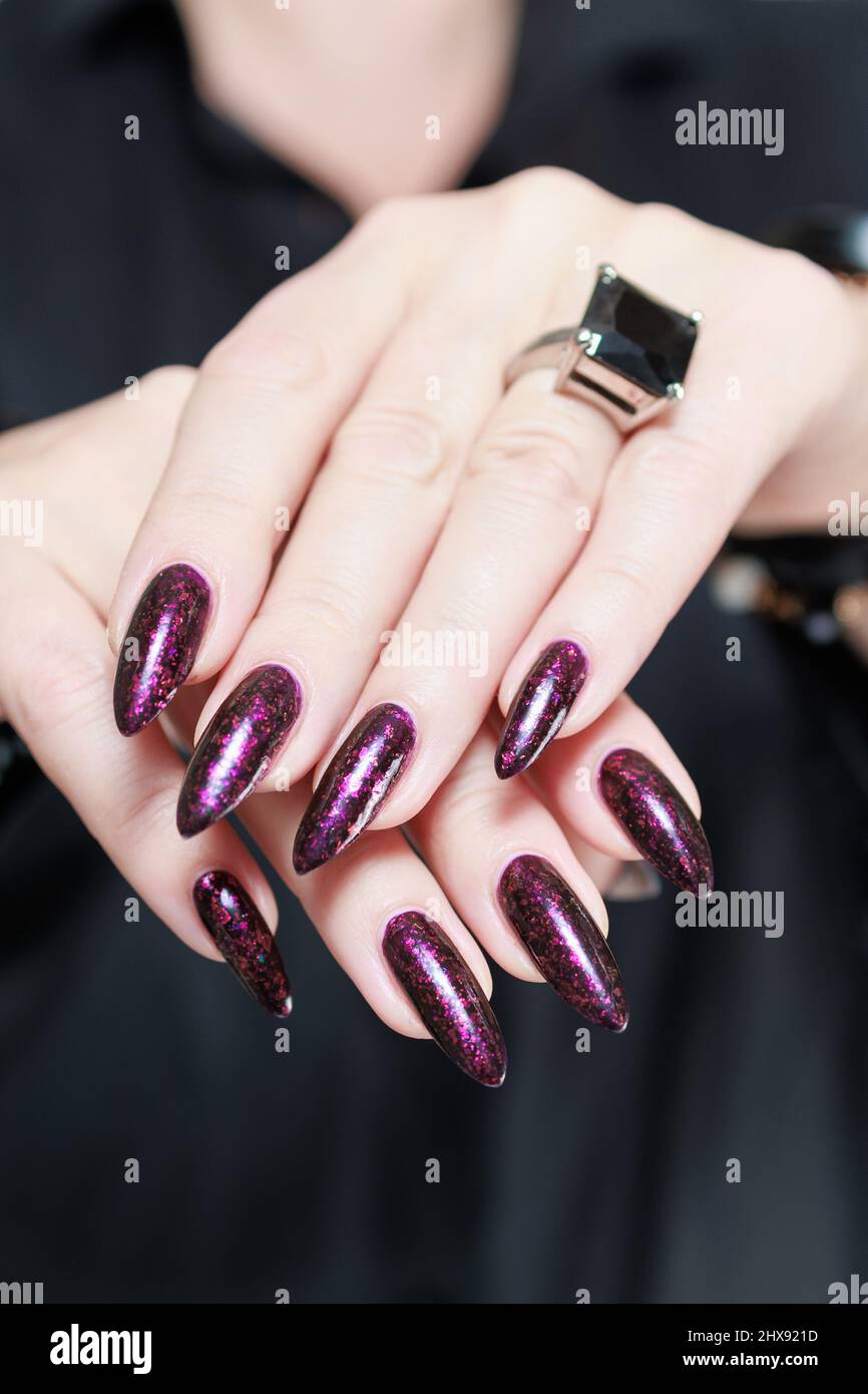 Manos femeninas con uñas largas y manicura púrpura borgoña sosteniendo una  botella de esmalte de uñas Fotografía de stock - Alamy