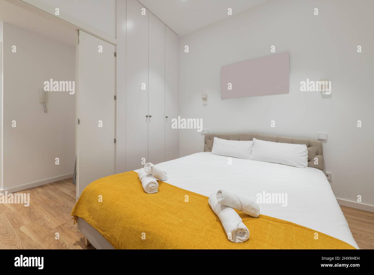 Dormitorio con cama king con edredón blanco, amarilla pequeña, armario empotrado blanco, toallas enrolladas en la cama y de madera en una t corta Fotografía de stock - Alamy