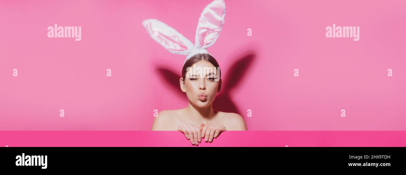Bandera de Pascua con mujer conejita. Primer plano retrato de una chica alegre con orejas rosas, beso de aire. Mujer conejita de Pascua. Foto de stock
