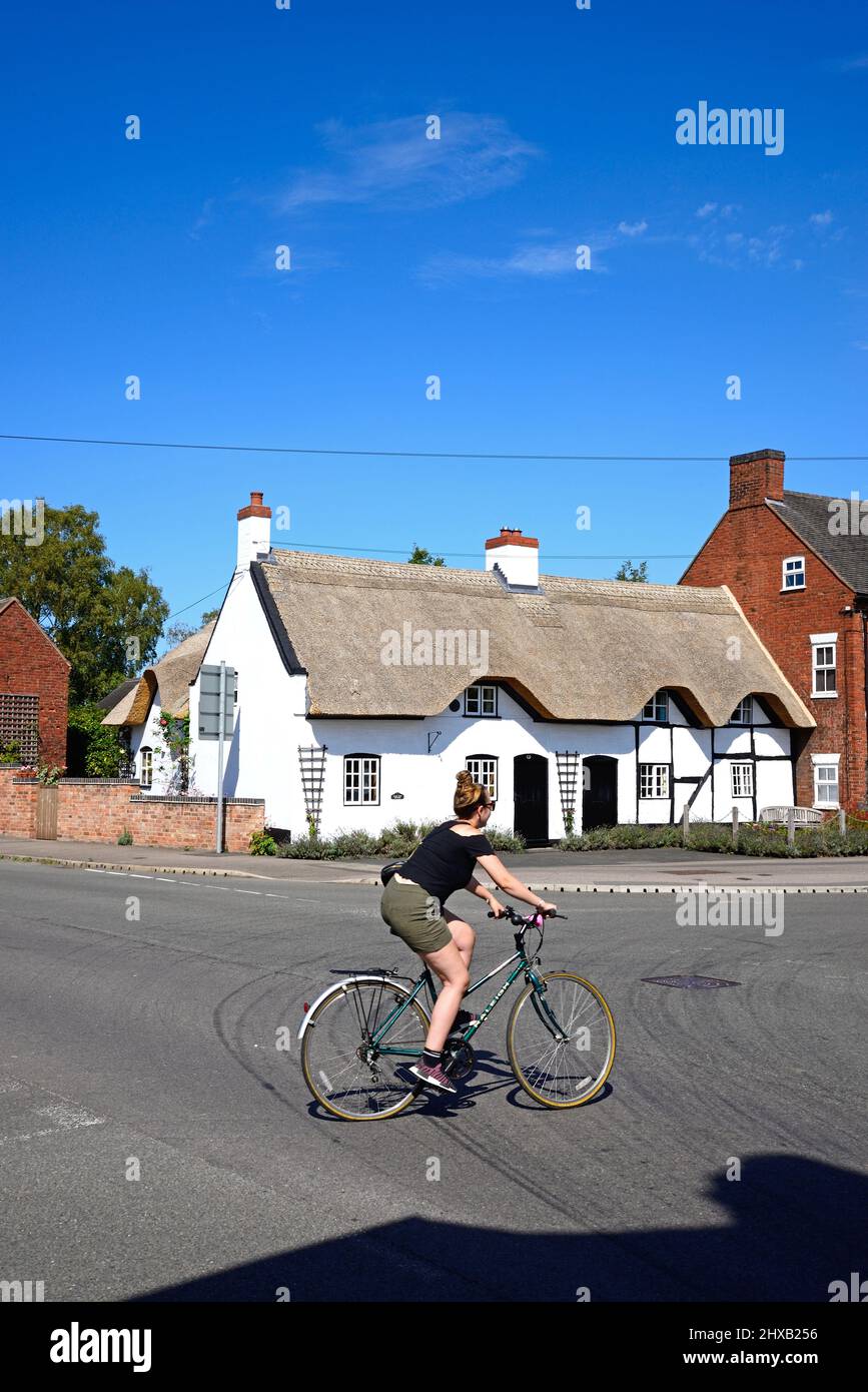 Bonita casa de campo tradicional de paja encalada inglesa en el centro del pueblo con un ciclista en primer plano, Kings Bromley, Staffordshire, Inglaterra, Foto de stock