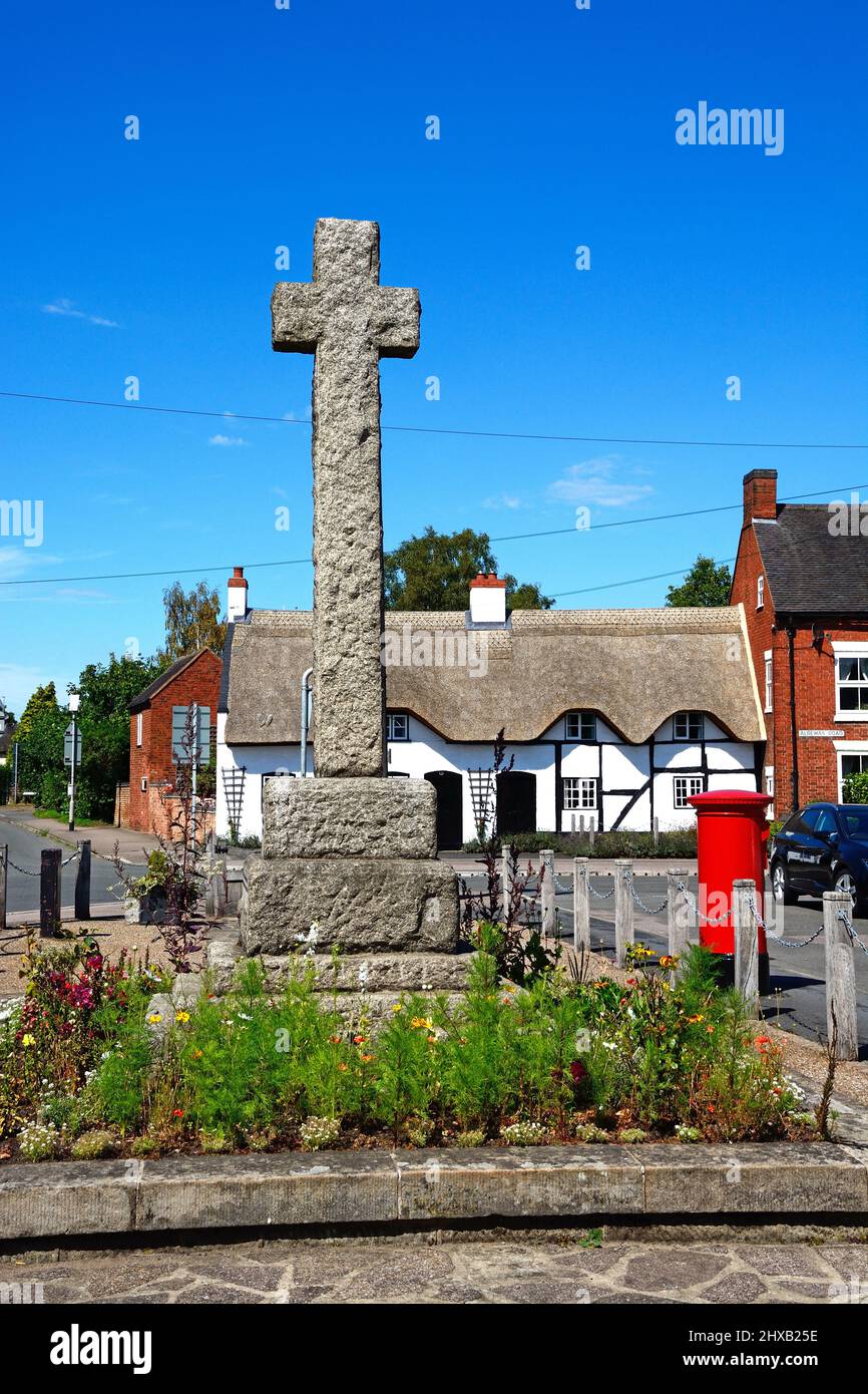 Cruce de piedra en el centro del pueblo con una casa de campo de paja y tradicional caja de correos rojos en la parte trasera, Kings Bromley, Staffordshire, Inglaterra, Reino Unido, Europa. Foto de stock