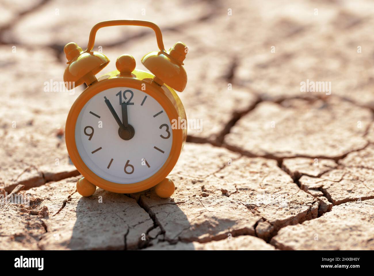 Despertador con cinco minutos antes de las doce en punto sobre el suelo árido agrietado. Concepto de cambio climático o calentamiento global. Foto de stock