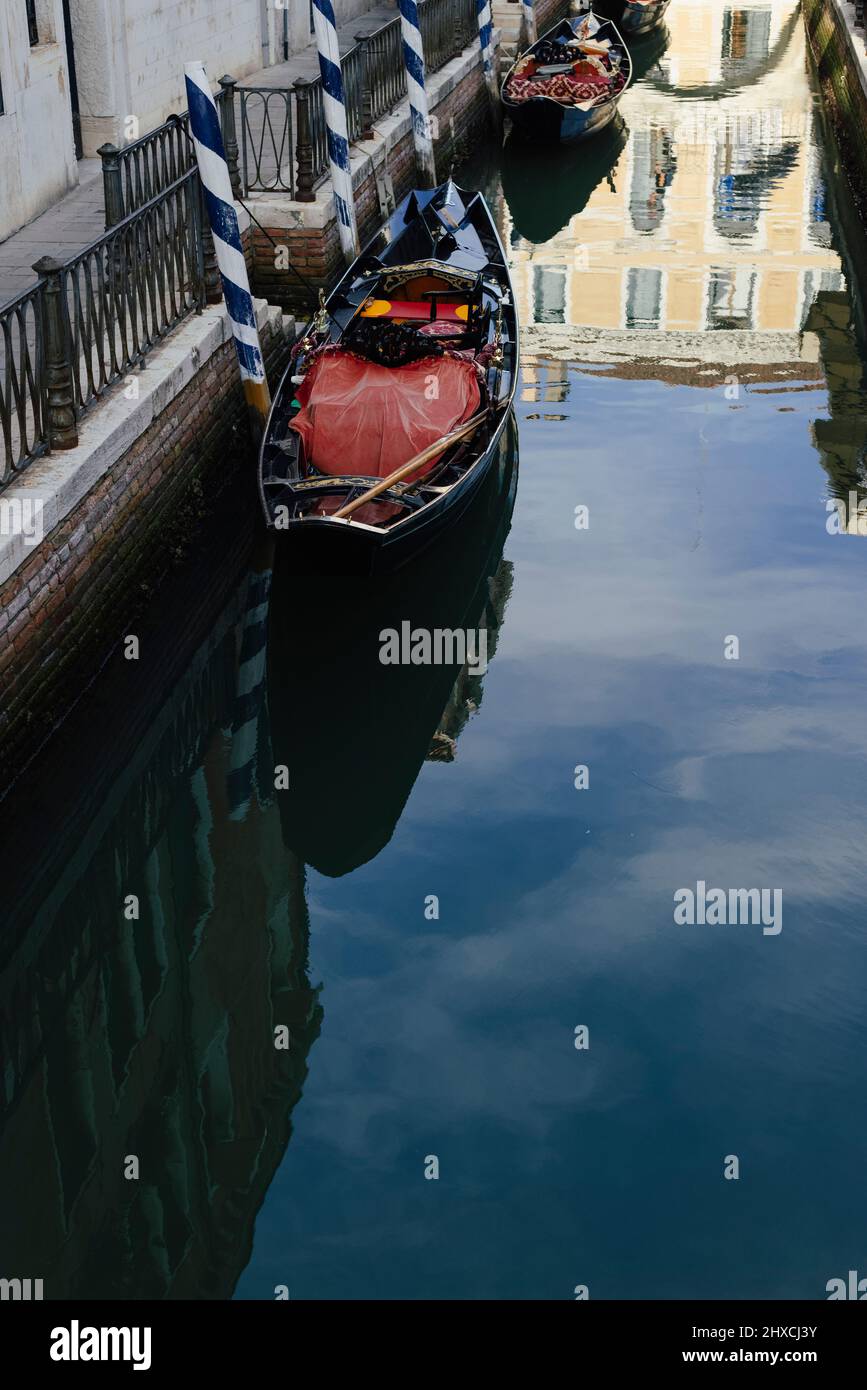 Vista de góndolas abandonadas con el reflejo de un edificio veneciano en la superficie del agua en Venecia, Italia Foto de stock