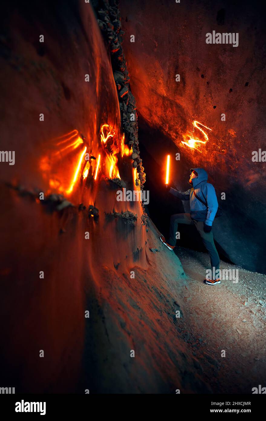 Hombre de turismo sosteniendo una lámpara de incandescencia roja en una profunda cueva de hielo glacial estrecha con explorar el glaciar de montaña de invierno en Kazajstán Foto de stock