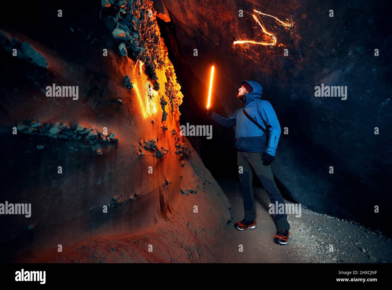 Hombre de turismo sosteniendo una lámpara de incandescencia roja en una profunda cueva de hielo glacial estrecha con explorar el glaciar de montaña de invierno en Kazajstán Foto de stock