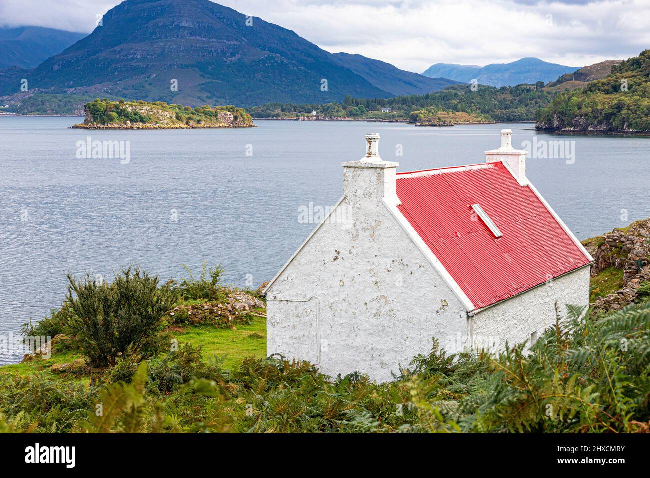 un pequeño croft con un techo de hierro corrugado rojo en las orillas del lago Shieldaig en Ardheslaig, Highland, Escocia Reino Unido. Foto de stock