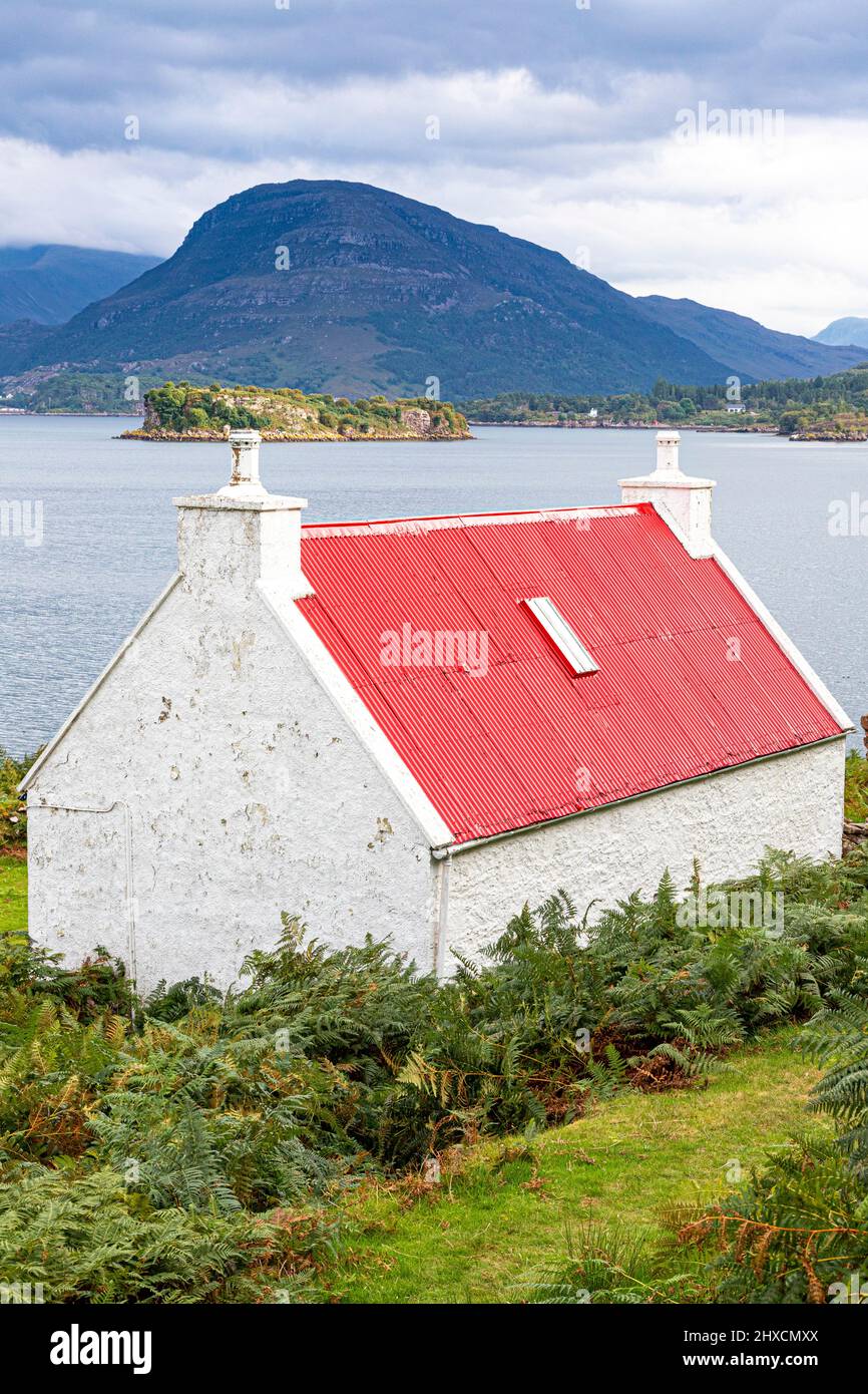 un pequeño croft con un techo de hierro corrugado rojo en las orillas del lago Shieldaig en Ardheslaig, Highland, Escocia Reino Unido. Foto de stock