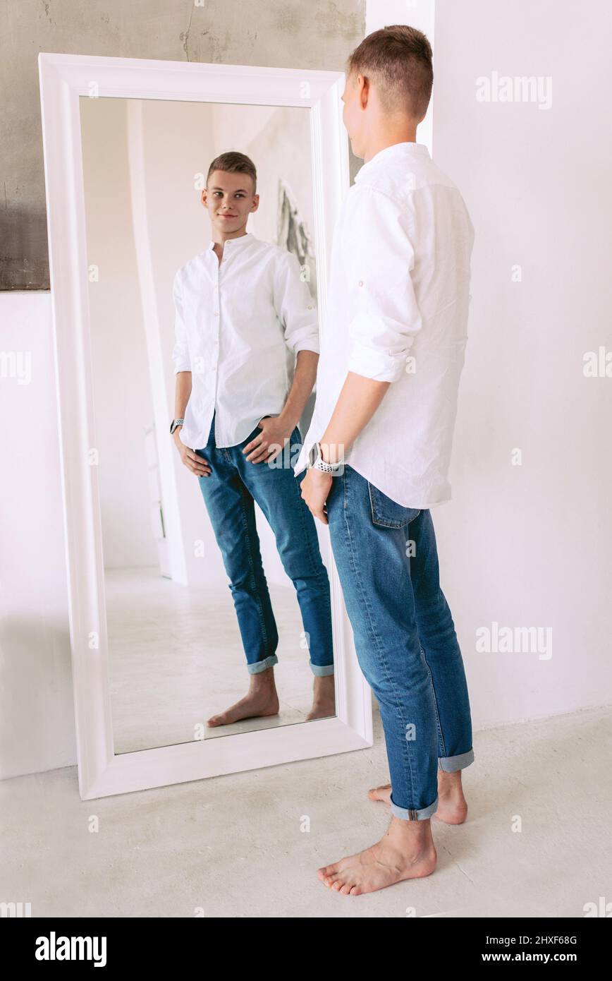 guapo hombre con camisa blanca y jeans azules junto al espejo interior.  Moda, concepto de estilo Fotografía de stock - Alamy