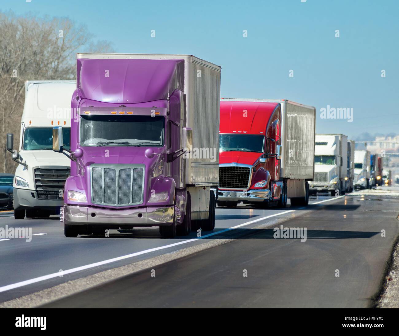 Disparo horizontal de un convoy multicolor de grandes camiones que ruedan por la interestatal. Foto de stock