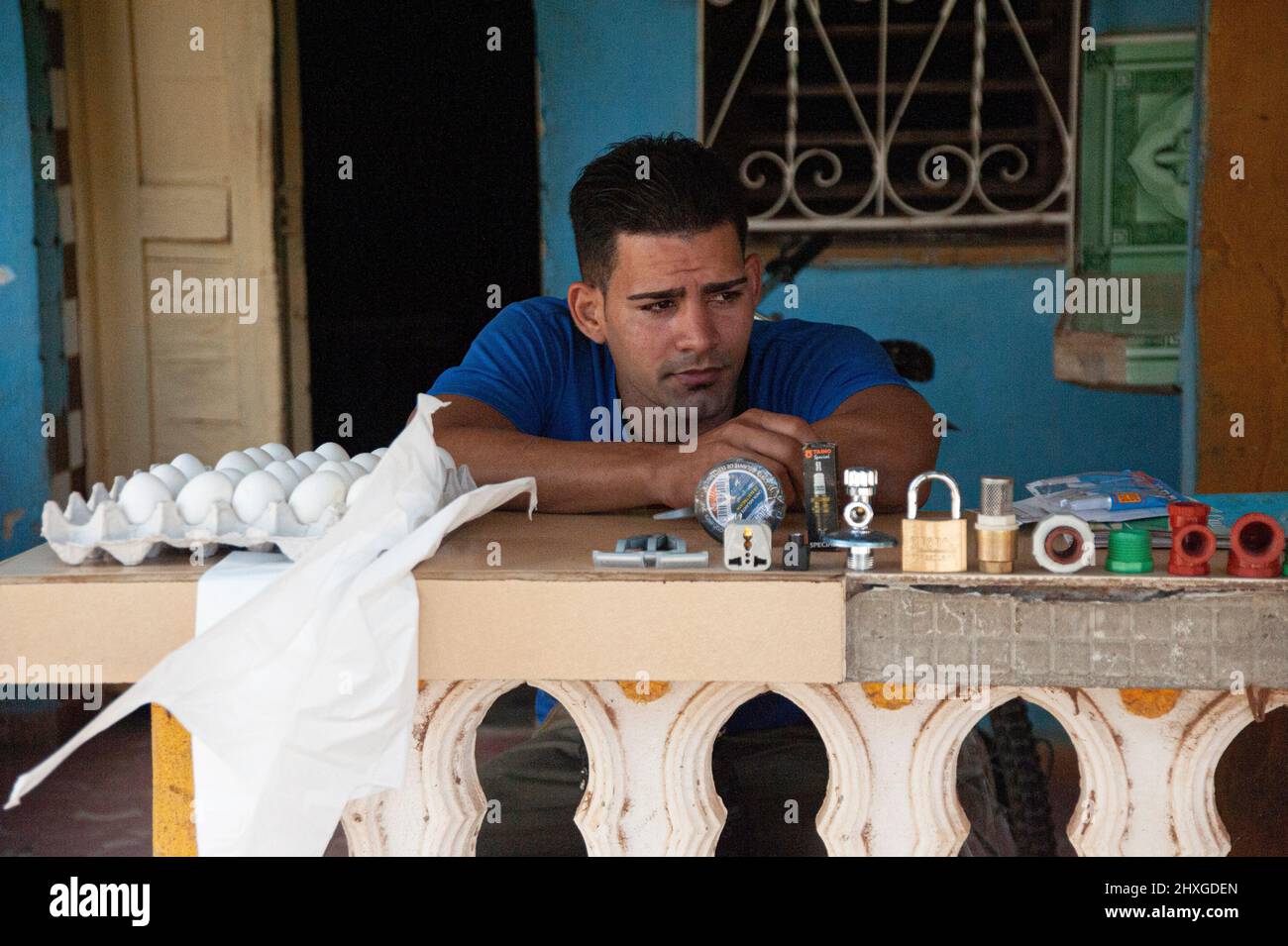 El hombre se sienta en el porche de su casa en Trinidad, Cuba, vendiendo huevos y un favorito de artículos para los clientes. Foto de stock