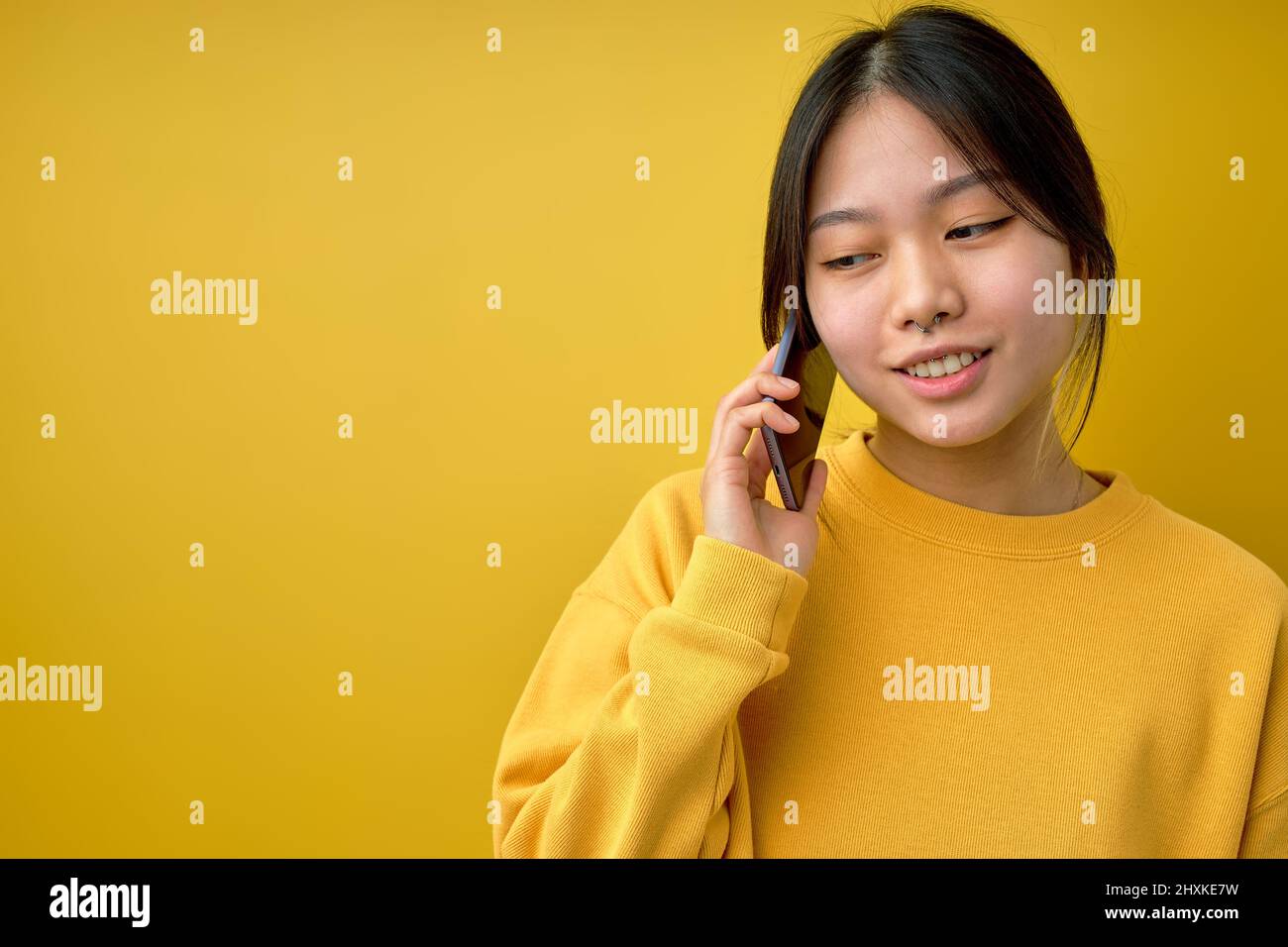 Bonita joven mujer china de pie aislado en fondo amarillo sosteniendo un smartphone hablando con alguien por teléfono. Espacio de copia. Chino moderno Femenino Us Foto de stock