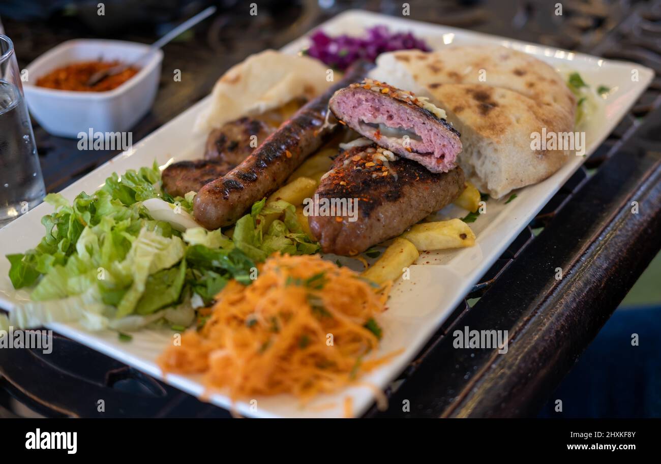 Diferentes tipos de carne a la parrilla o a la parrilla, albóndigas con queso y salchichas con ensalada de verduras en el plato Foto de stock
