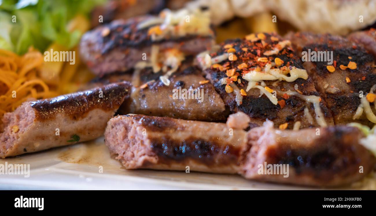 Diferentes tipos de carne a la parrilla o a la parrilla, albóndigas con queso y salchichas con ensalada de verduras en el plato Foto de stock