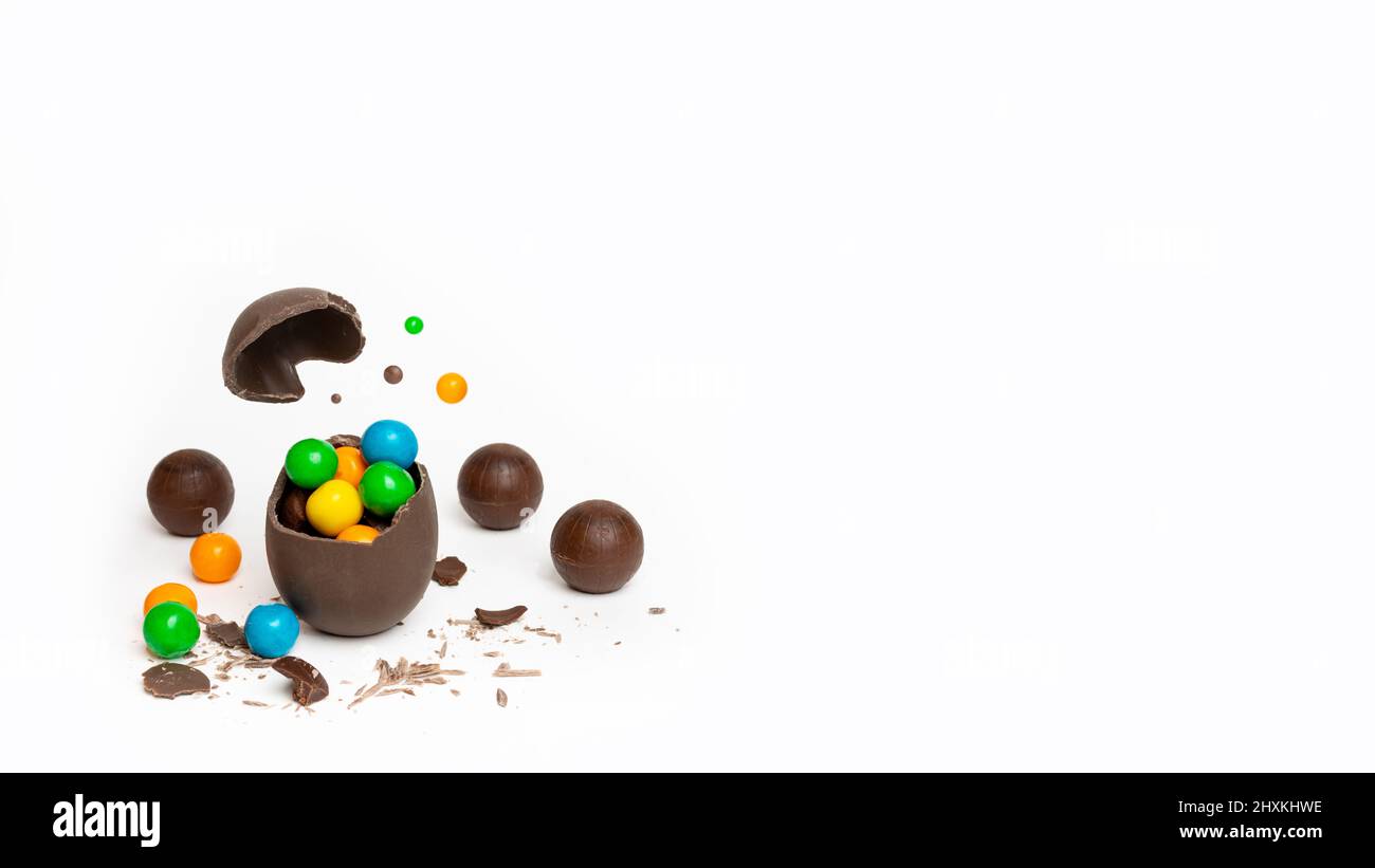 Huevo de pascua de chocolate craqueado con caramelos redondos y coloridos sobre fondo blanco, espacio de copia, pancarta. Un huevo de chocolate con leche rota Foto de stock