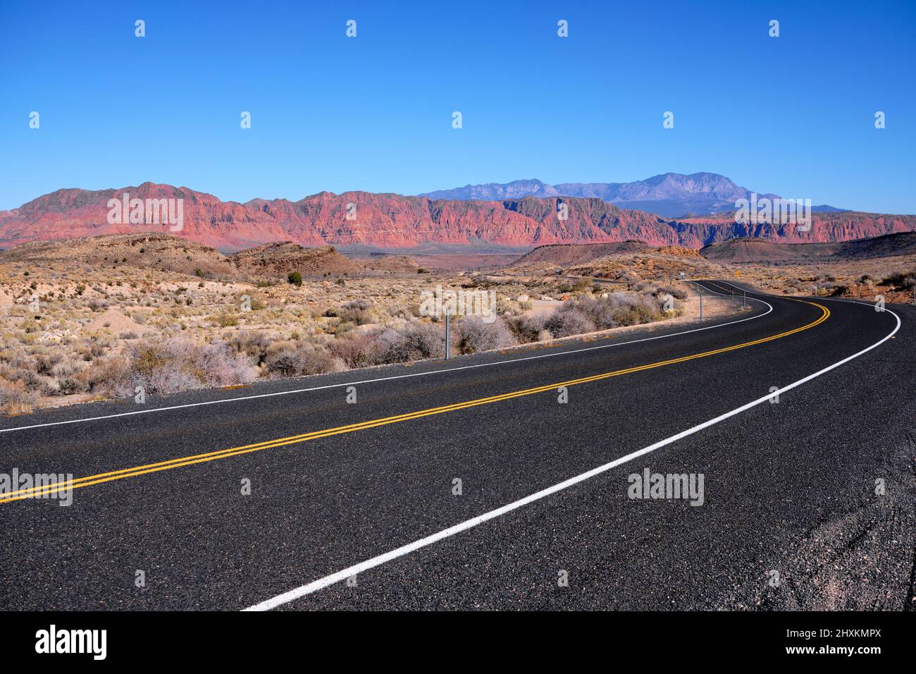 Conducción en el pavimento suave y negro de la antigua autopista 91 en el suroeste de Utah. En el horizonte está el país de Red Rock bajo cielos azules y sin nubes Foto de stock