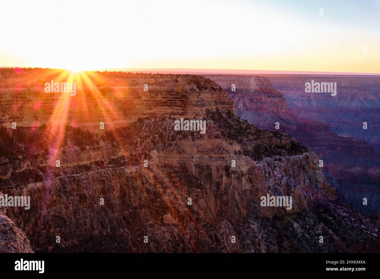 Cuando el sol se pone cerca de Hopi Point en el Parque Nacional del Gran Cañón, rayos de sol rojos, naranjas y amarillos se extienden por debajo del borde del cañón Foto de stock