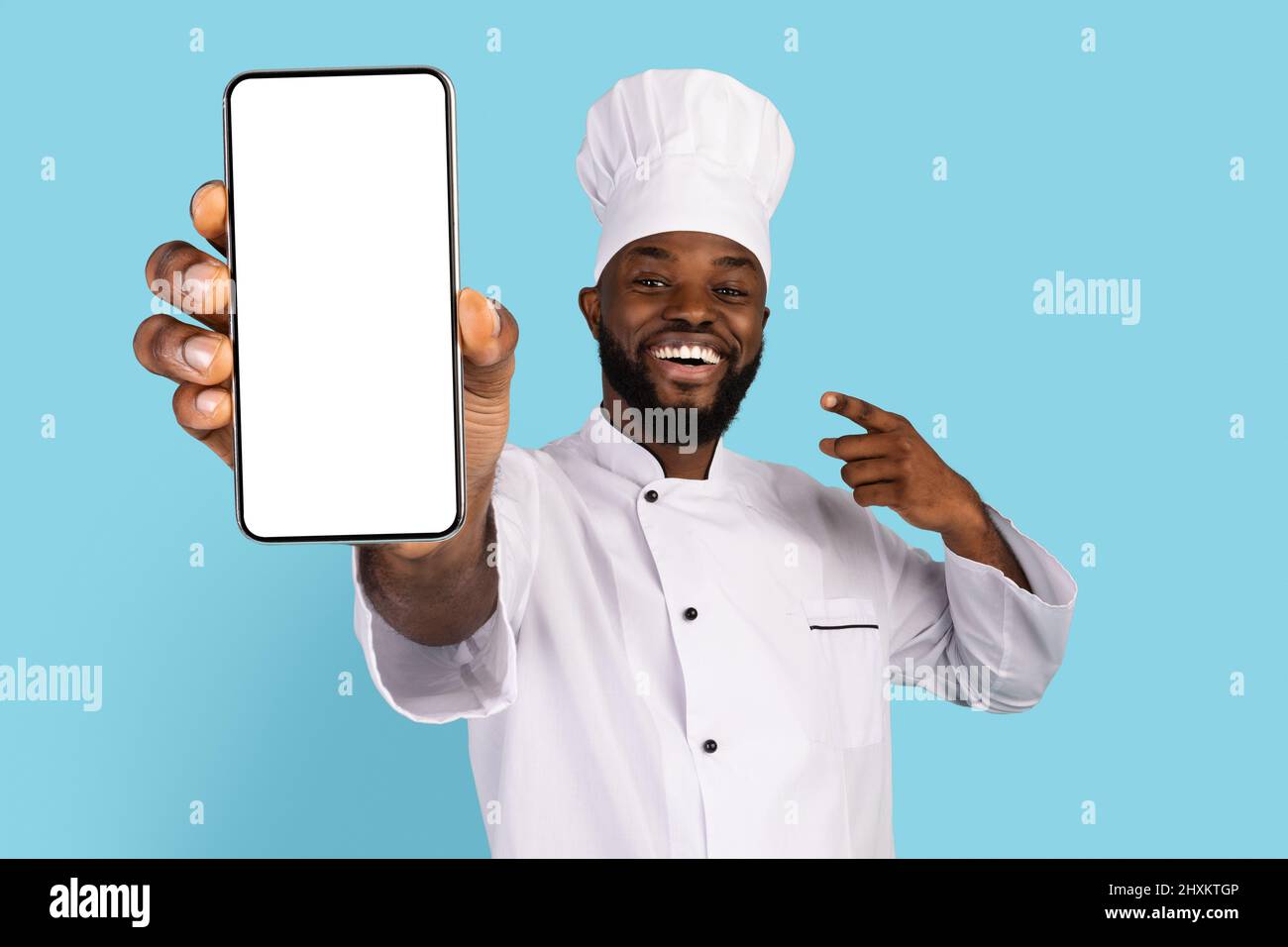 Aplicación de cocina Emocionado chef negro apuntando a Blank smartphone en su mano Foto de stock