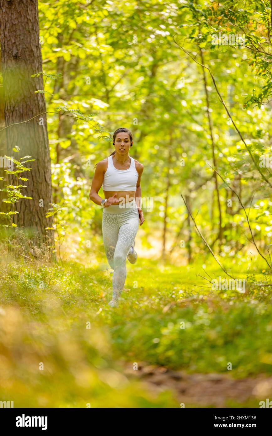 FIT Woman Running in Woodland durante el entrenamiento de resistencia Foto de stock