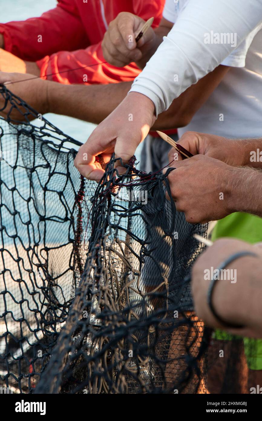 Grupo de pescadores reparando la red de pesca, trabajando con las manos cerca Foto de stock