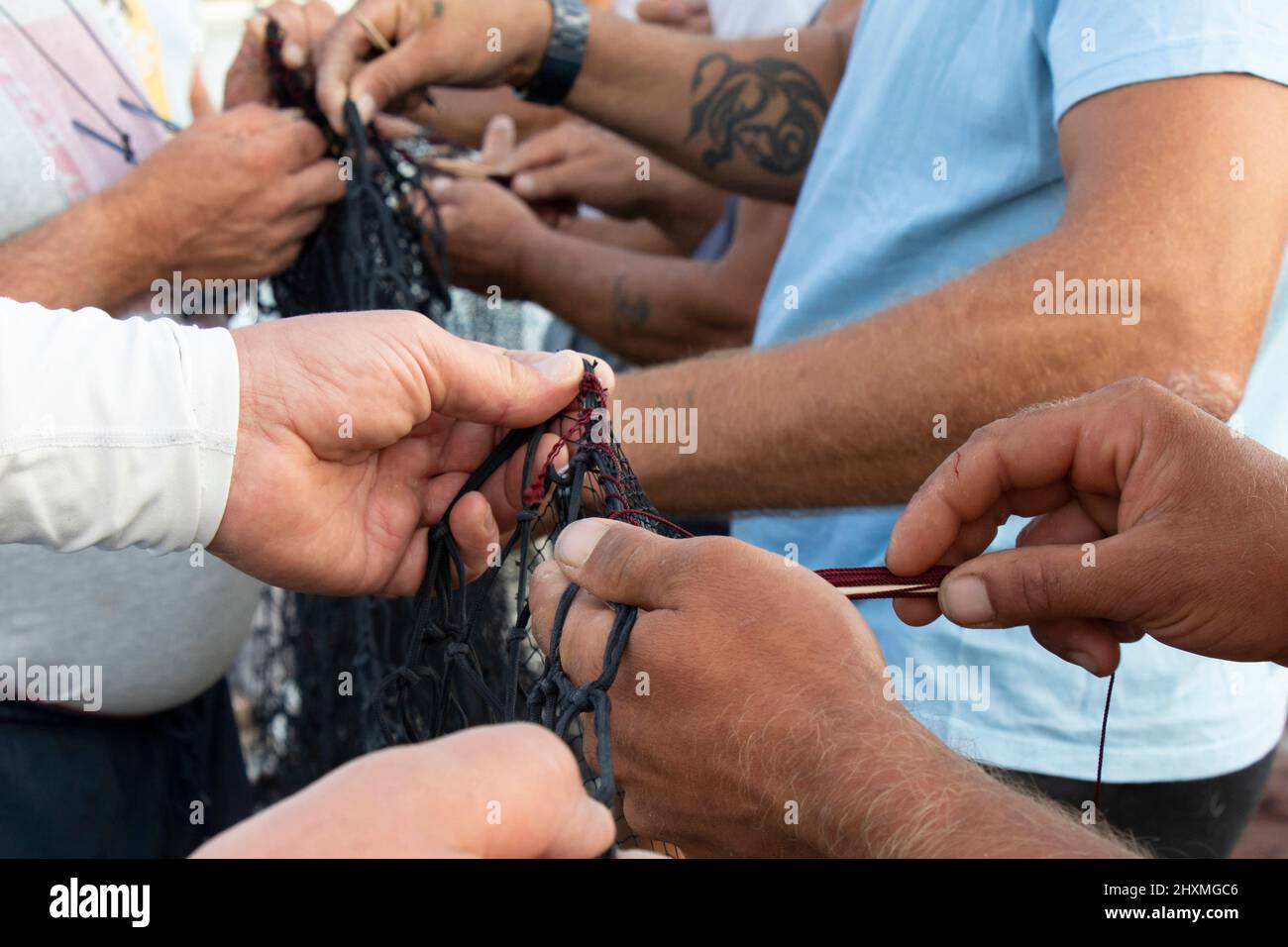 Tribunj, Croacia - 23 de agosto de 2021: Grupo de pescadores reparando la red de pesca, trabajando con las manos de cerca de detalles Foto de stock