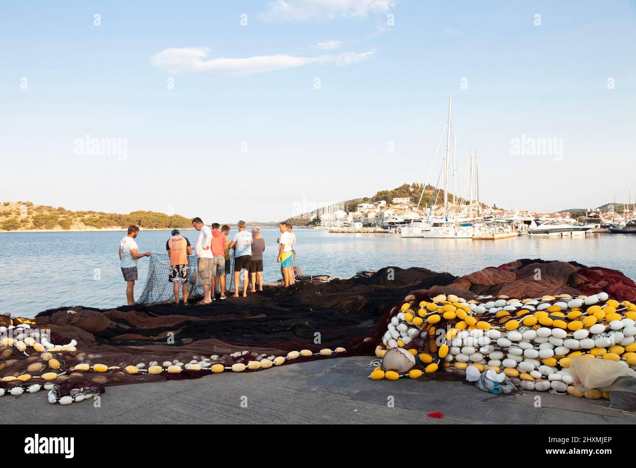 Tribunj, Croacia - 23 de agosto de 2021: Grupo de pescadores reparando la red de pesca en el muelle costero Foto de stock
