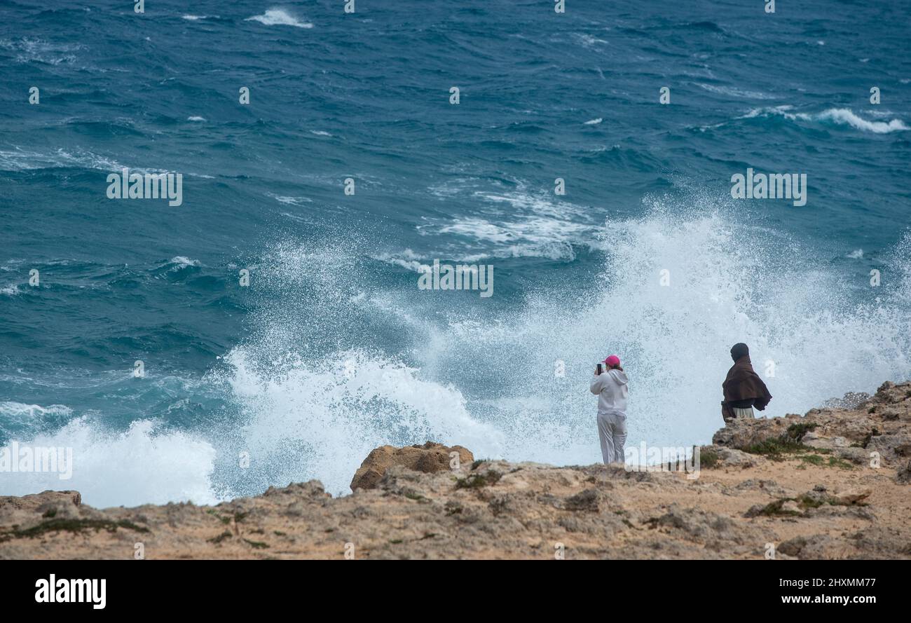 Gente en una costa rocosa en el océano tormentoso. Peligrosas olas ventosas que rompen en las rocas Foto de stock