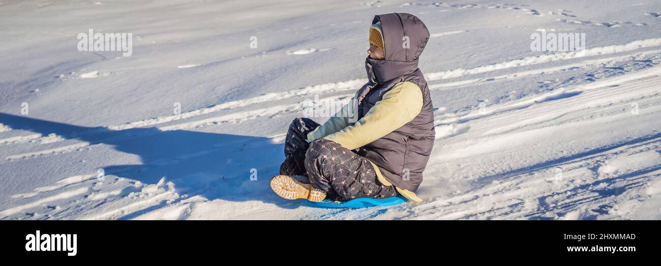 BANNER, FORMATO LARGO Feliz mujer divertirse durante el balanceo por la ladera de la montaña en trineo. Deportes de invierno con nieve. Gente montando un trineo Foto de stock