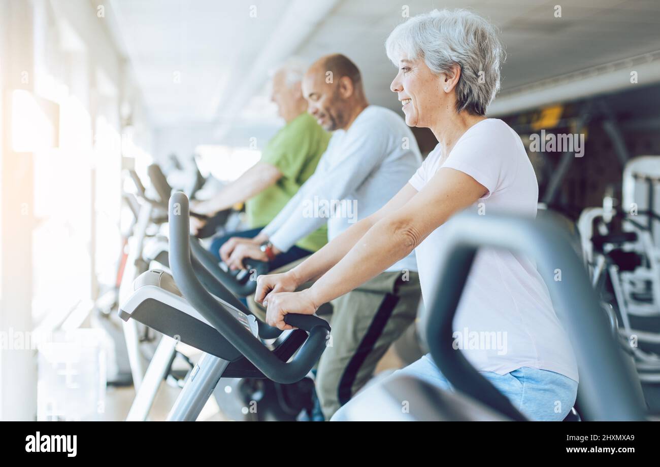 Ajuste a las personas mayores en bicicletas estáticas de fitness en el gimnasio Foto de stock